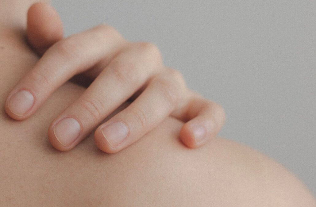 Eine Hand liegt auf der Schulter. Die Finger zeigen auf den Schmerz